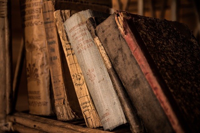 An image of old books leaning together on a shelf.